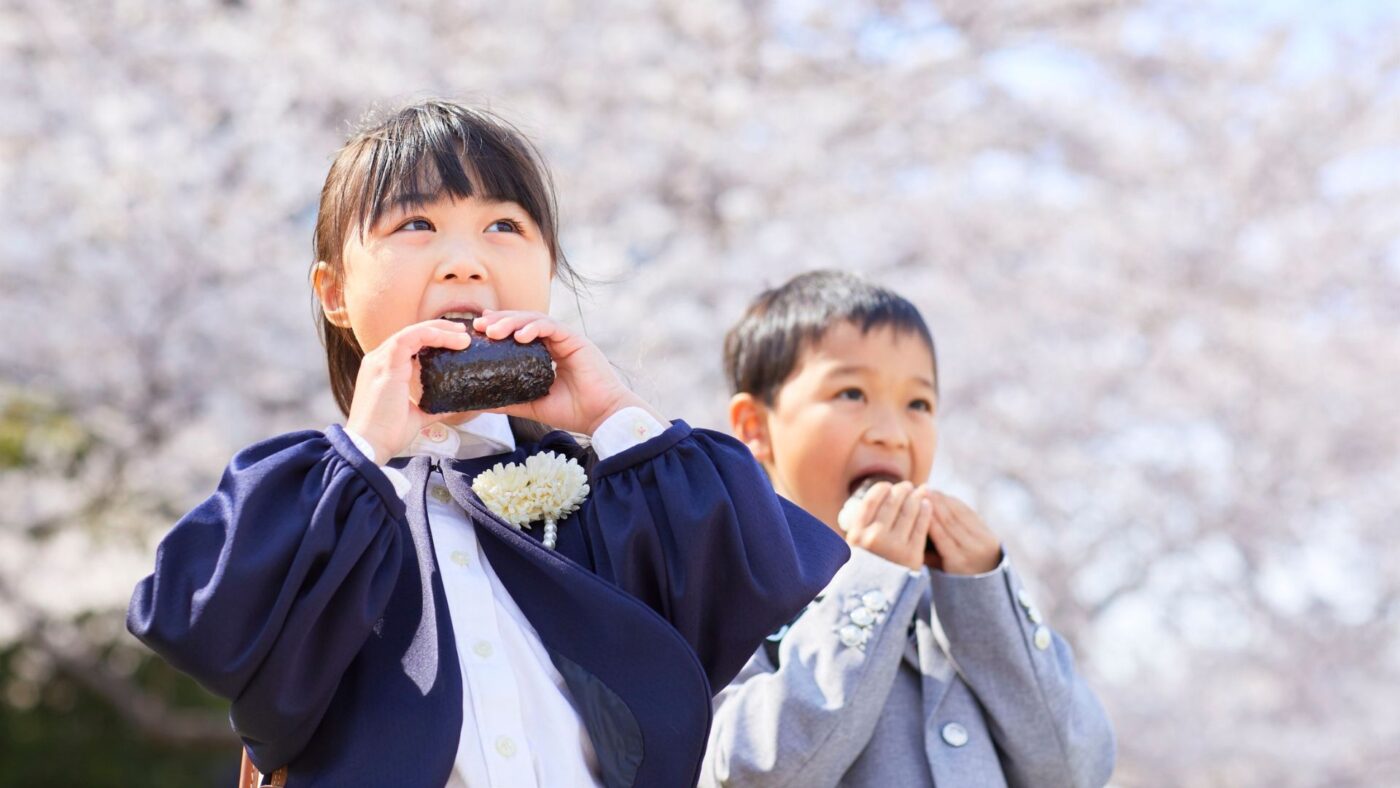 des enfants japonais mangent un onigiri devant des cerisiers en fleurs